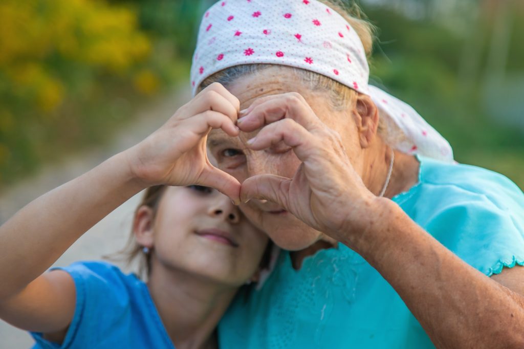 Grandmother and granddaughter make a heart with their hands. Selective focus.