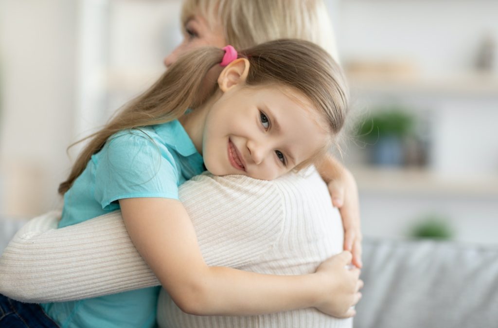 Happy mature woman and granddaughter hugging at home